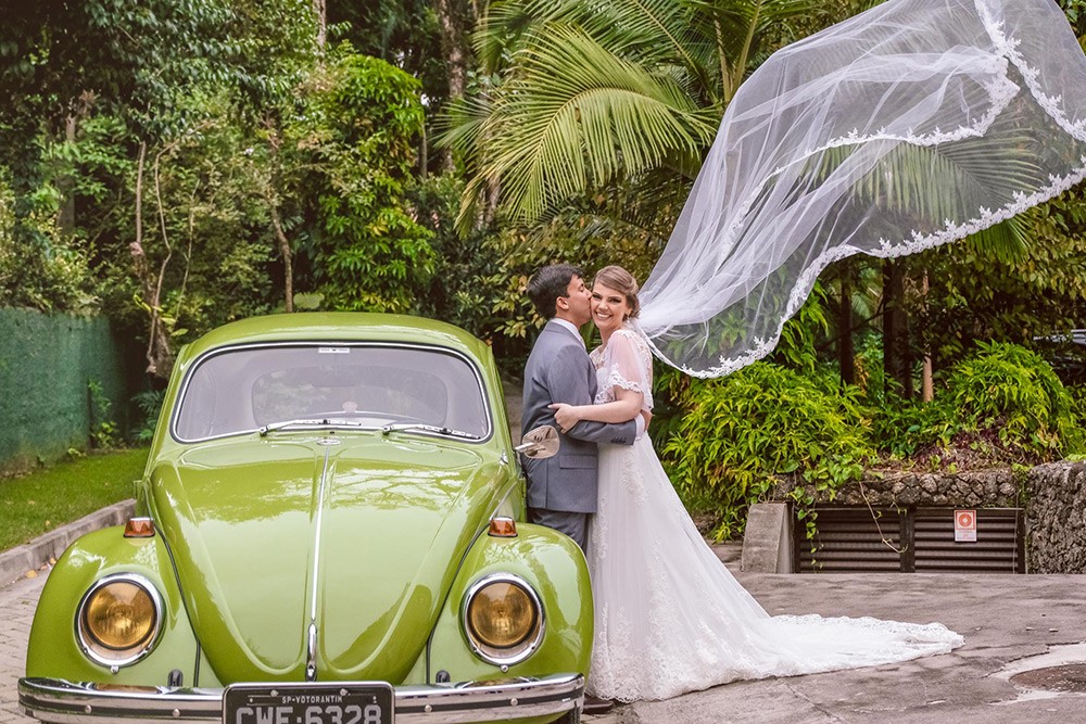noivos posando ao frente a um fusca após a cerimônia do casamento