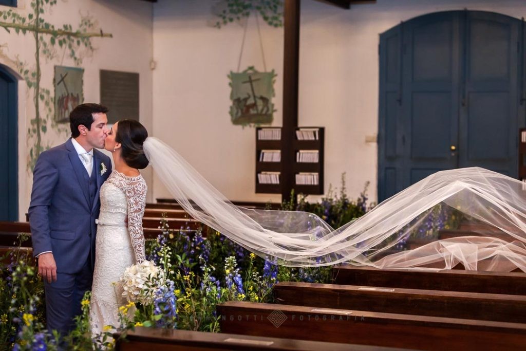 Casal se beijando após a cerimônia. O vestido da noiva tem um véu longo.